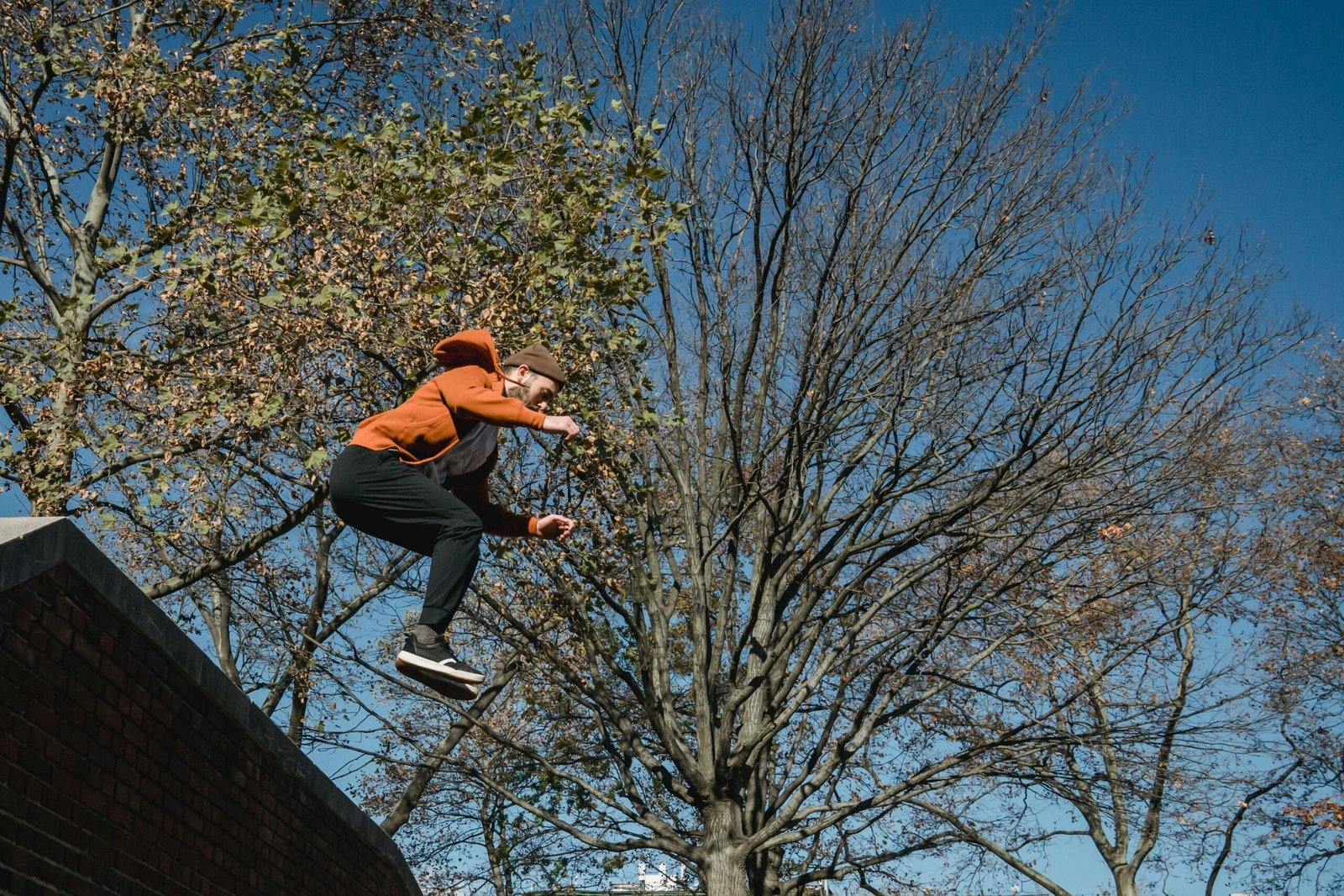 A traceur in baggy pants and hoodie jumping from a brick wall, showing the freedom of movement baggy parkour clothing allows.