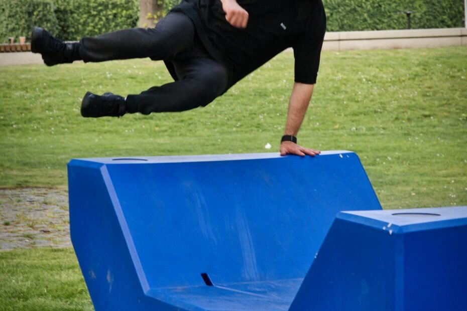 A traceur vaulting a purpose-built blue parkour obstacle set on grass in a public park.