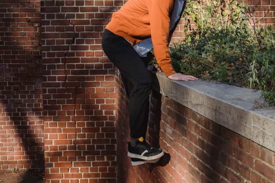 A traceur climbing up a brick wall with bare hands gripping the top edge.