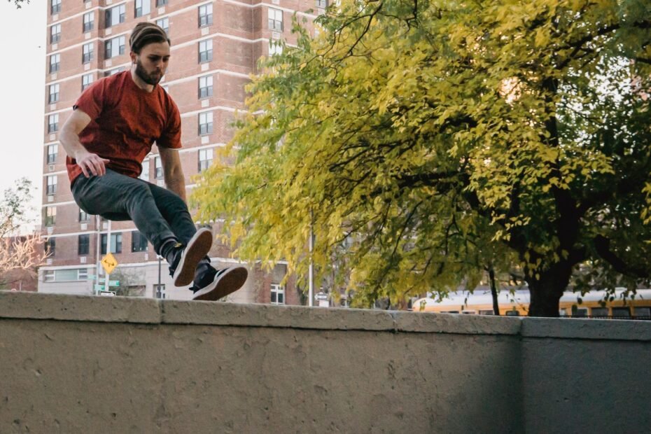 A traceur jumping over a concrete wall on a city street with trees and apartment buildings behind.