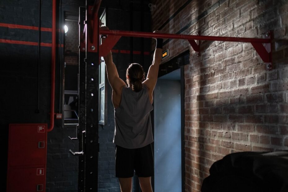 A man hanging from a red wall-mounted pull-up bar bolted to a brick wall with angled support brackets.