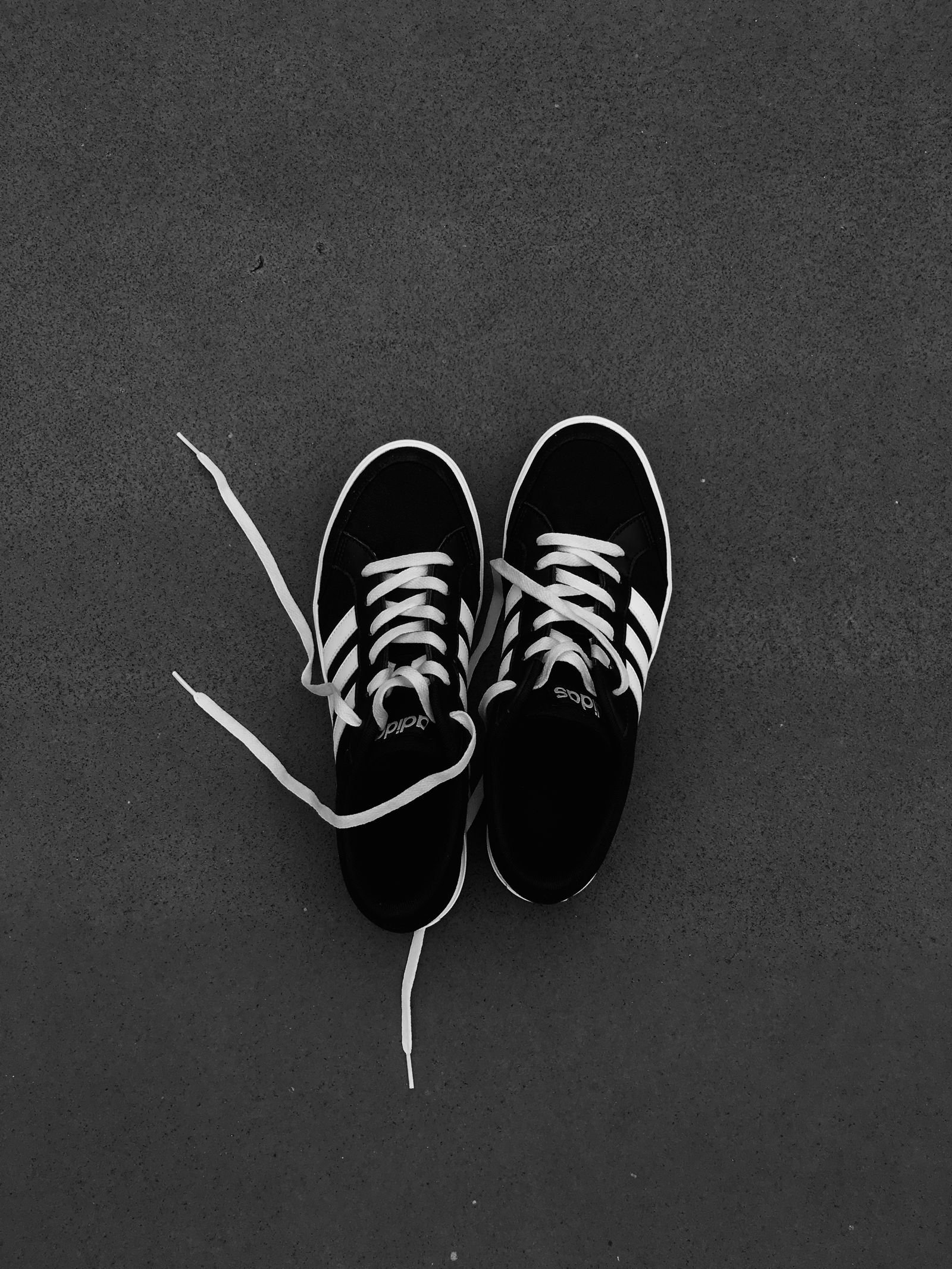 A pair of black canvas trainers with white laces and soles on a dark grey background.