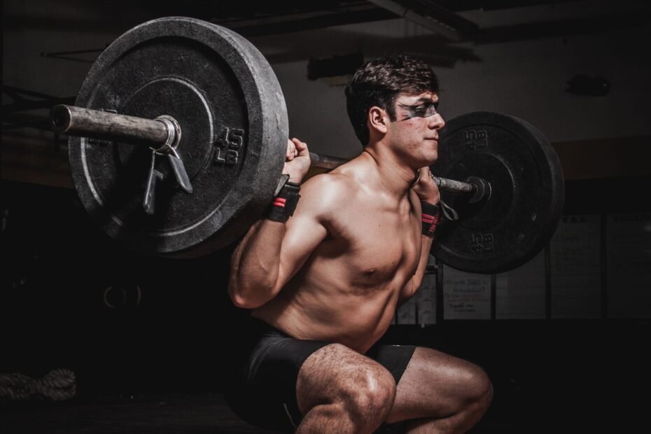 A man in a deep barbell back squat in a dark gym.