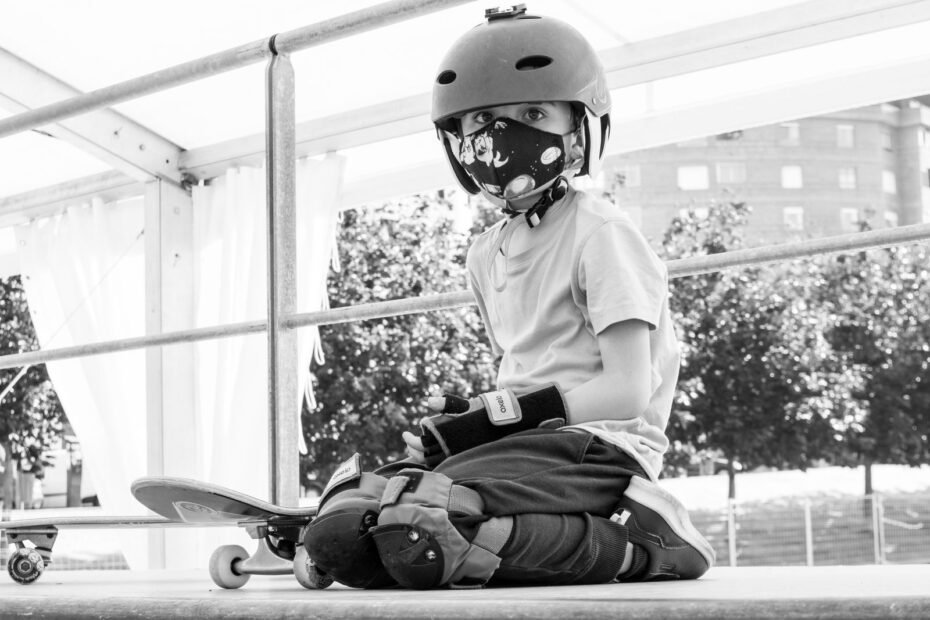 A young skater wearing a helmet and knee pads, kneeling next to a skateboard.