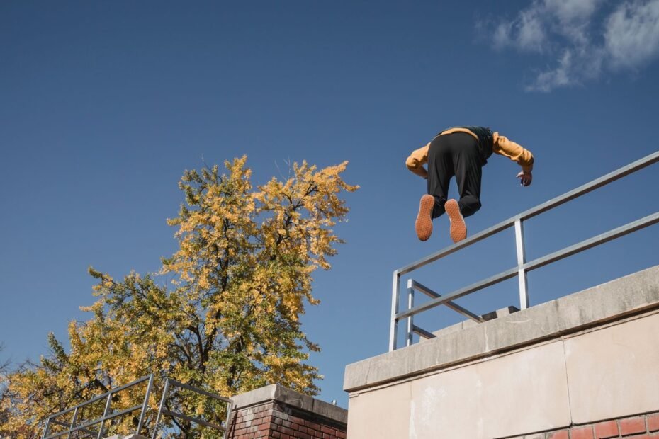 A traceur in mid-air over a metal railing on top of a wall, against a blue sky.
