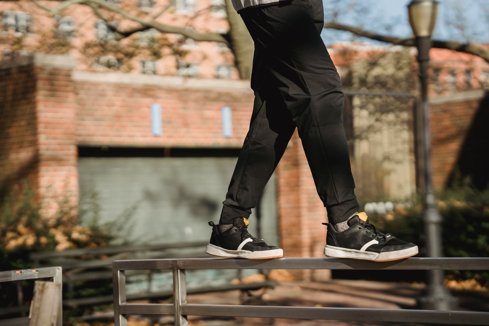 Close-up of a traceur's feet in black trainers balancing on a low metal rail in a park.