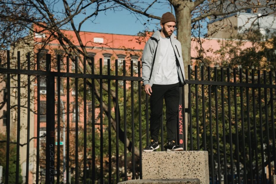 A traceur in a grey jacket standing on a concrete pillar beside tall black iron railings.