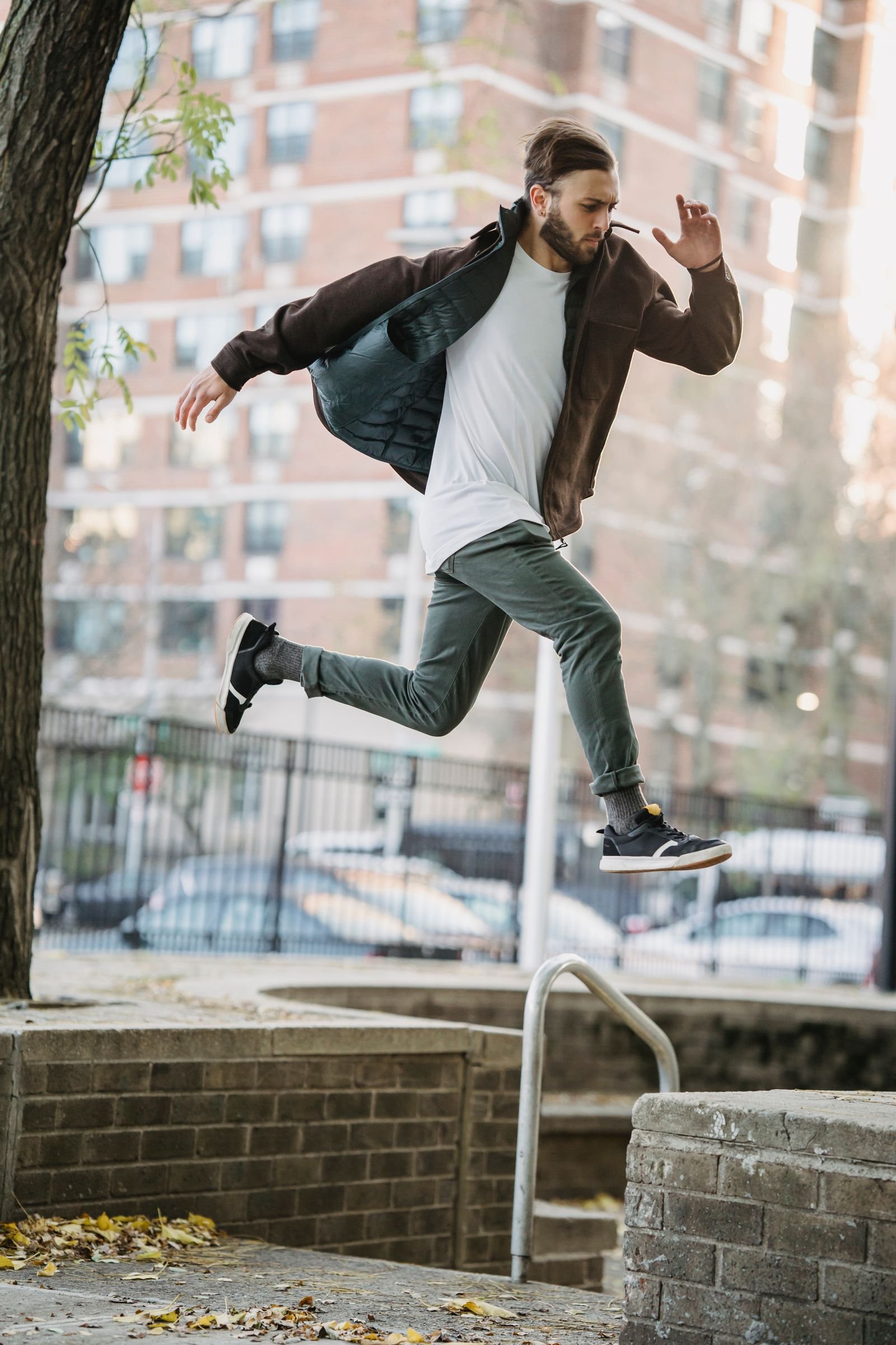 A traceur in a dark jacket mid-air in a running leap above a low brick ledge.