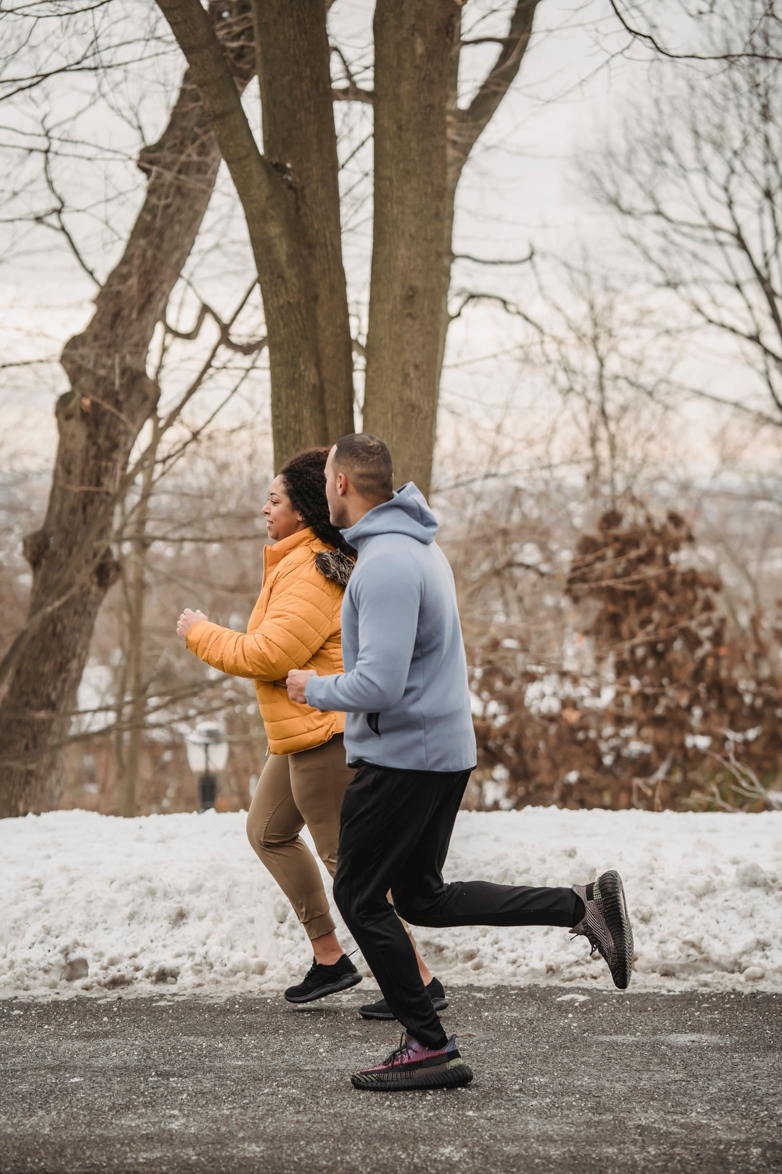 Two people in hoodies and jackets running on a path with snow on the ground.